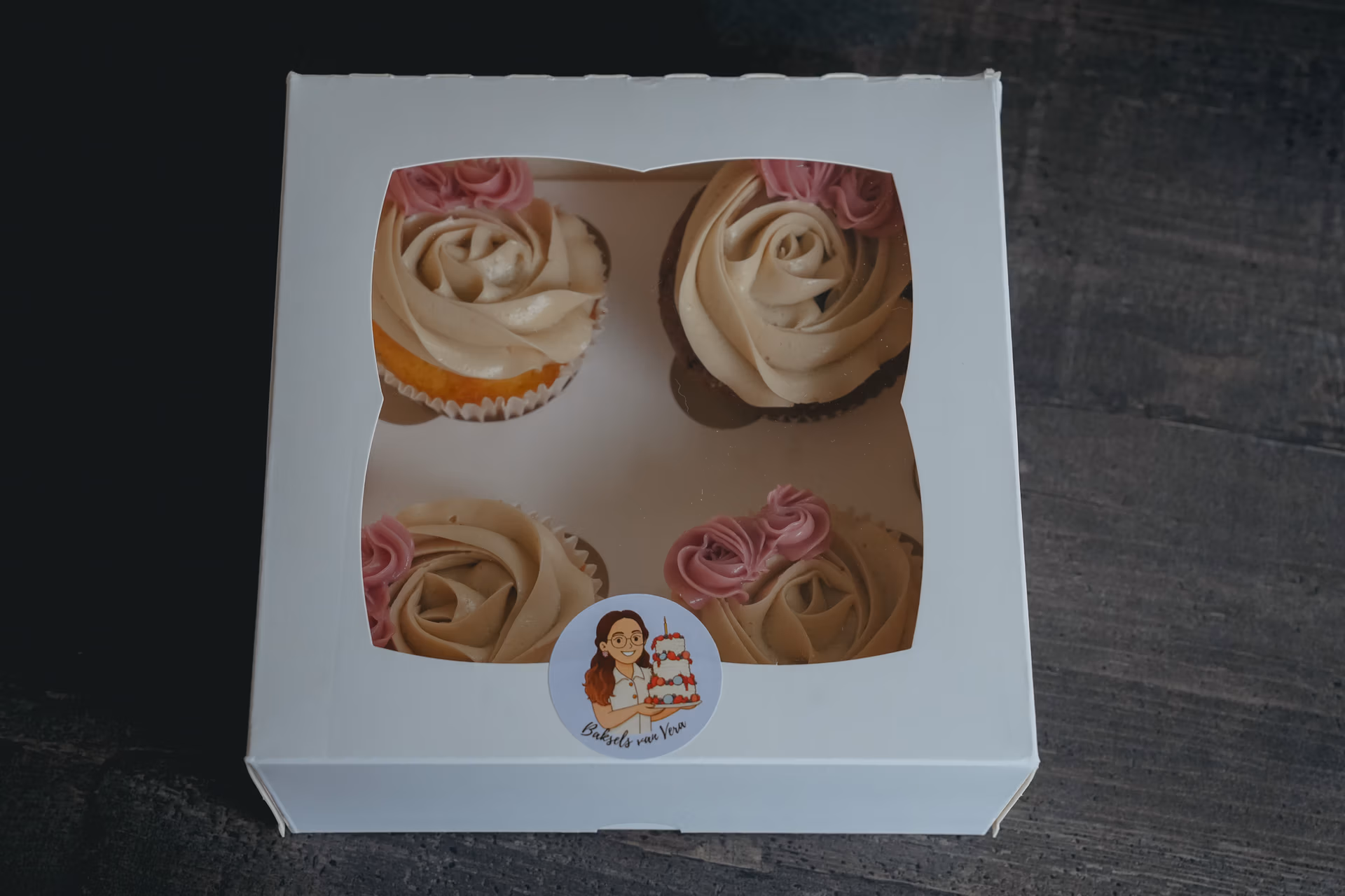 Doos met vier cupcakes met botercrème‑rozen en roze accenten, voorzien van een Baksels van Vera‑sticker.
