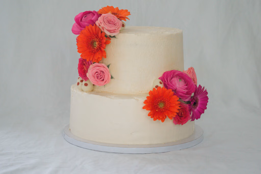 Tweelaagse witte bruidstaart met verse bloemen zoals gerbera’s, rozen en ranonkels.