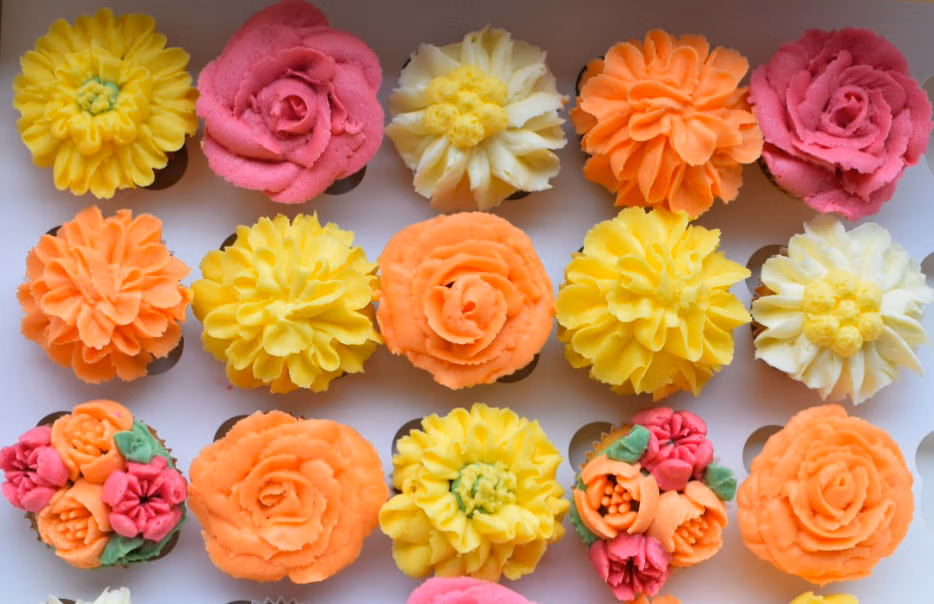 Cupcakes met bloemvormige botercrème in warme tinten zoals geel, oranje, roze en crème.