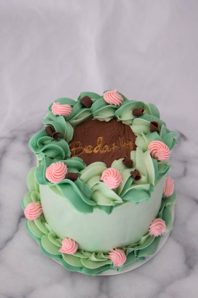 Ronde taart met lichtgroene botercrème, roze rozetten en gouden ‘Bedankt’-tekst op fondant cirkel