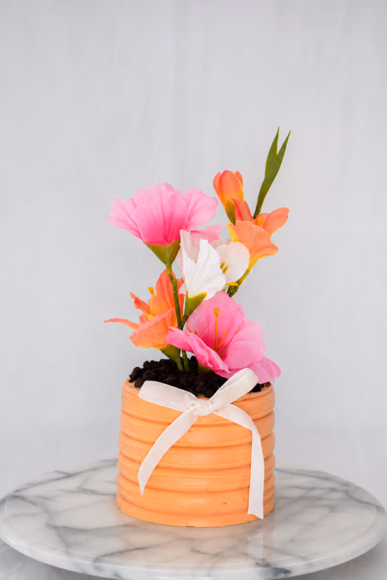 Bento taart in de vorm van een oranje bloempot met witte strik en kleurrijke bloemen bovenop.