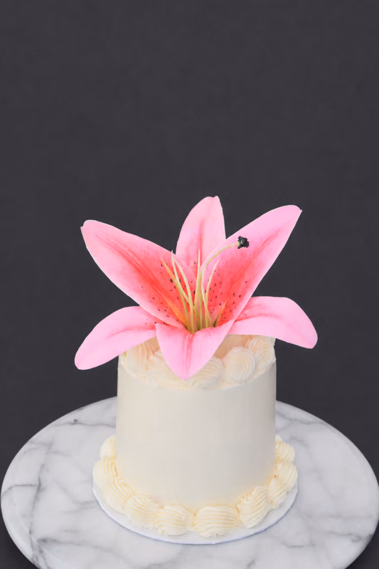 Witte bento taart met botercrème en grote roze lelie bovenop op marmeren taartplateau.