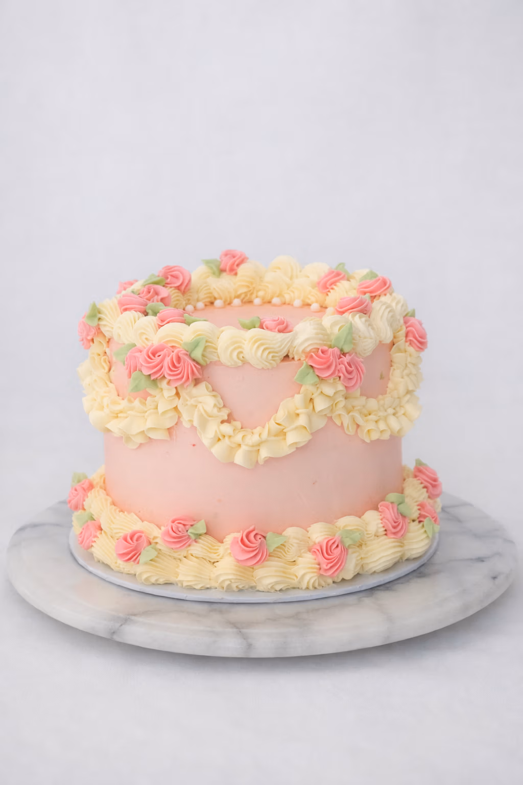 Roze vintage‑stijl taart met botercrème rozetten, swirls en garlandecoratie op een marmeren standaard.