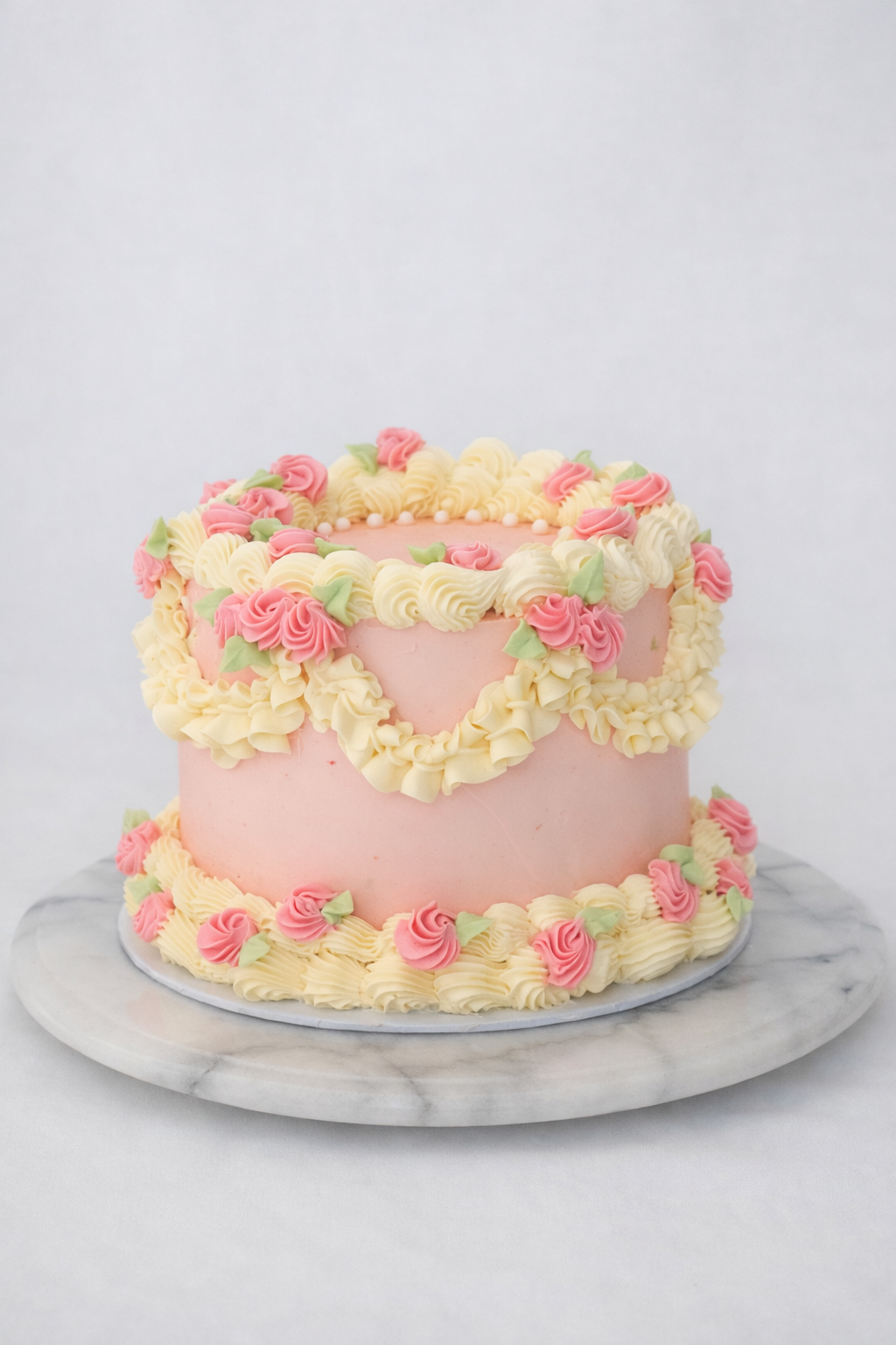 Roze vintage‑stijl taart met botercrème rozetten, swirls en garlandecoratie op een marmeren standaard.