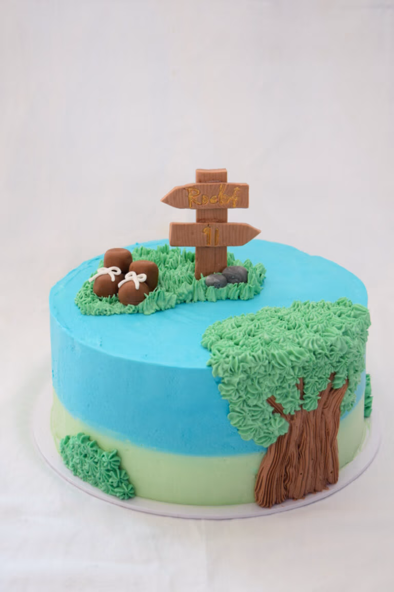 Taart met natuur‑ en wandeldecoratie, blauwe en groene botercrème, fondantlaarzen en een houten wegwijzer.