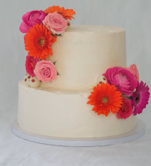 Tweelaagse witte bruidstaart met verse bloemen zoals gerbera’s, rozen en ranonkels.